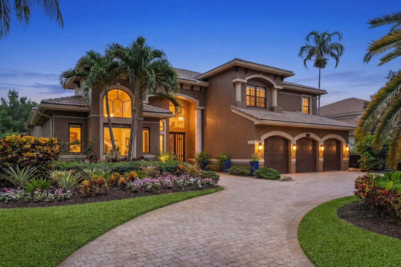 Twilight exterior of 2982 East Lake Vista Circle in Davie — glowing windows, tile roof and a curved paver driveway framed by palms against a deep-blue dusk sky